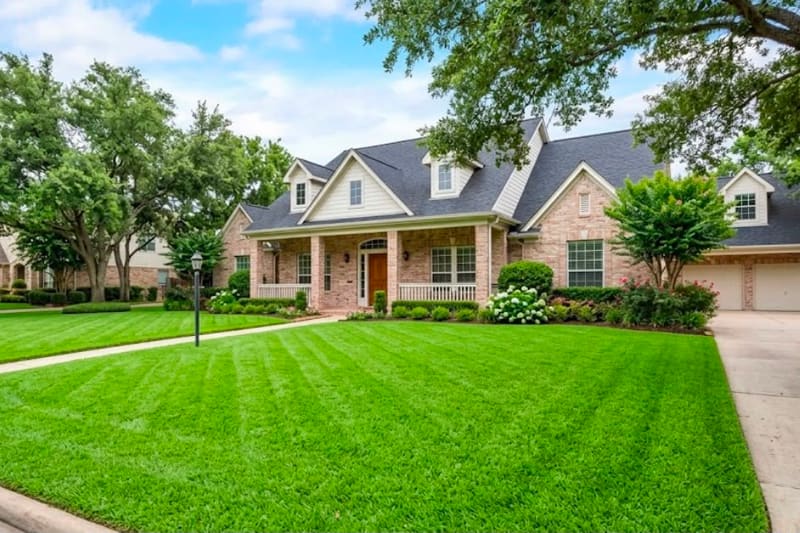 Wide front lawn with fresh mowing stripes and mature shade trees in front of a stone and brick home